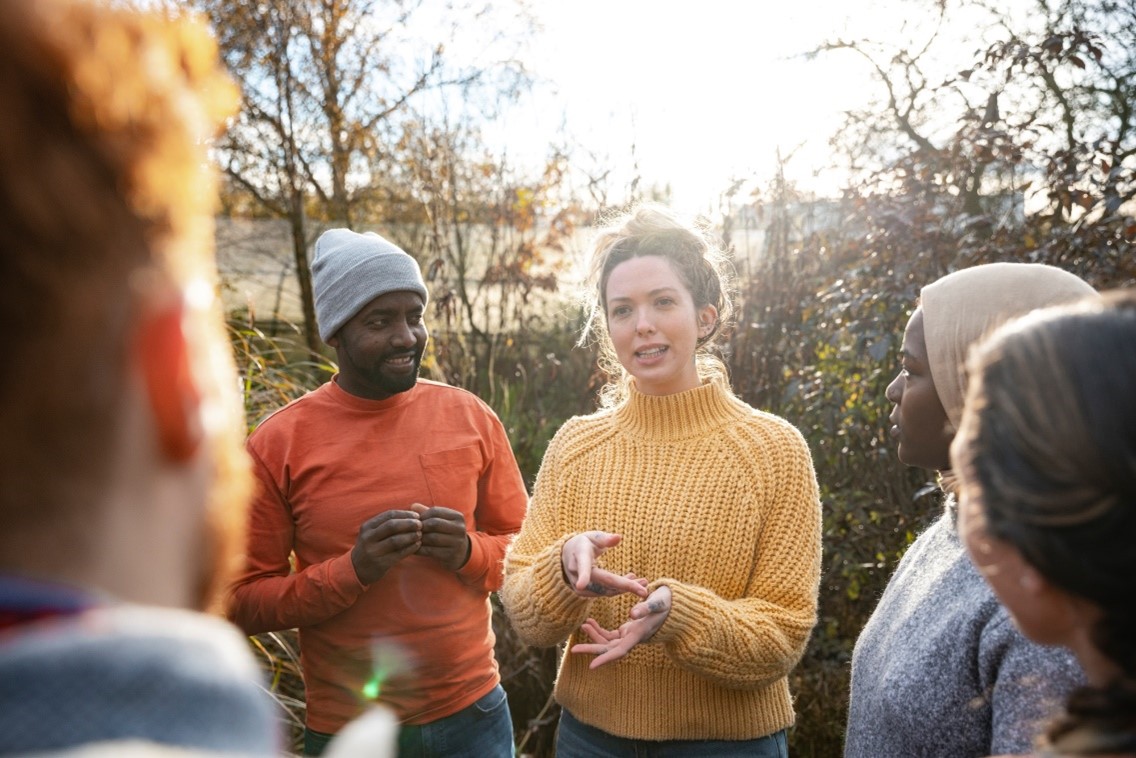 woman in yellow jumper and man in red jumper talking to group of people outside